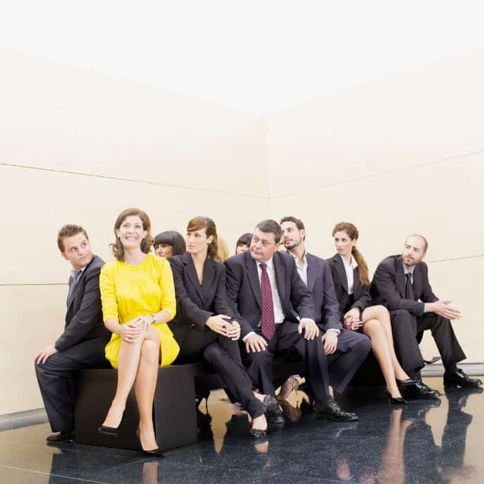 A business woman in a yellow dress sitting next to other business men and women who are all wearing black. How to describe your brand and stand out from the crowd.